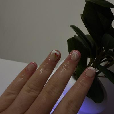 Sheer nude nails with delicate white french tips, tiny hearts, and gold accents